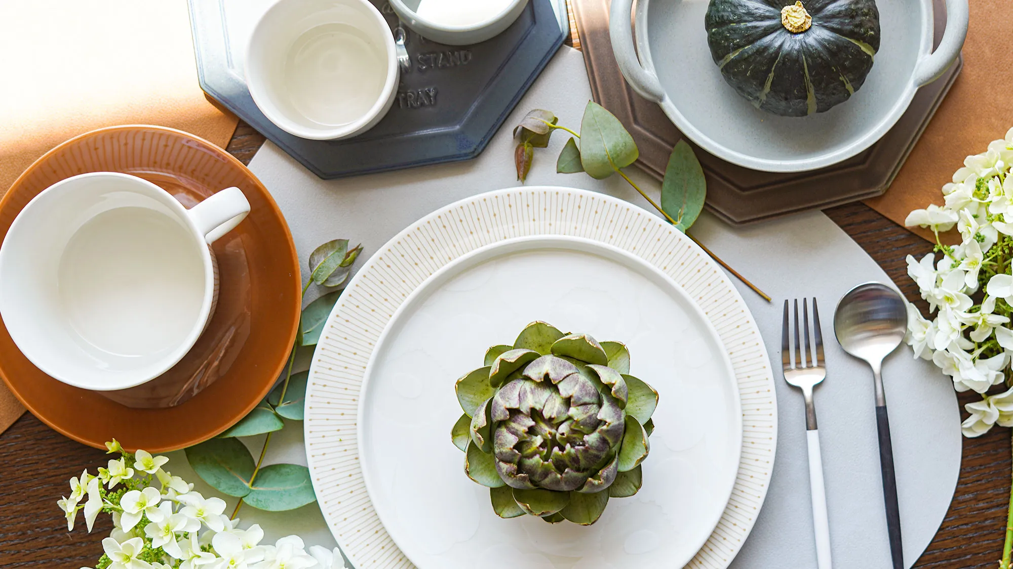 秋のテーブルコーディネート：ドットパターンの白プレートにアーティチョーク、テラコッタ色のC&S、かぼちゃを盛った器、ユーカリの葉、白いあじさい、カトラリー