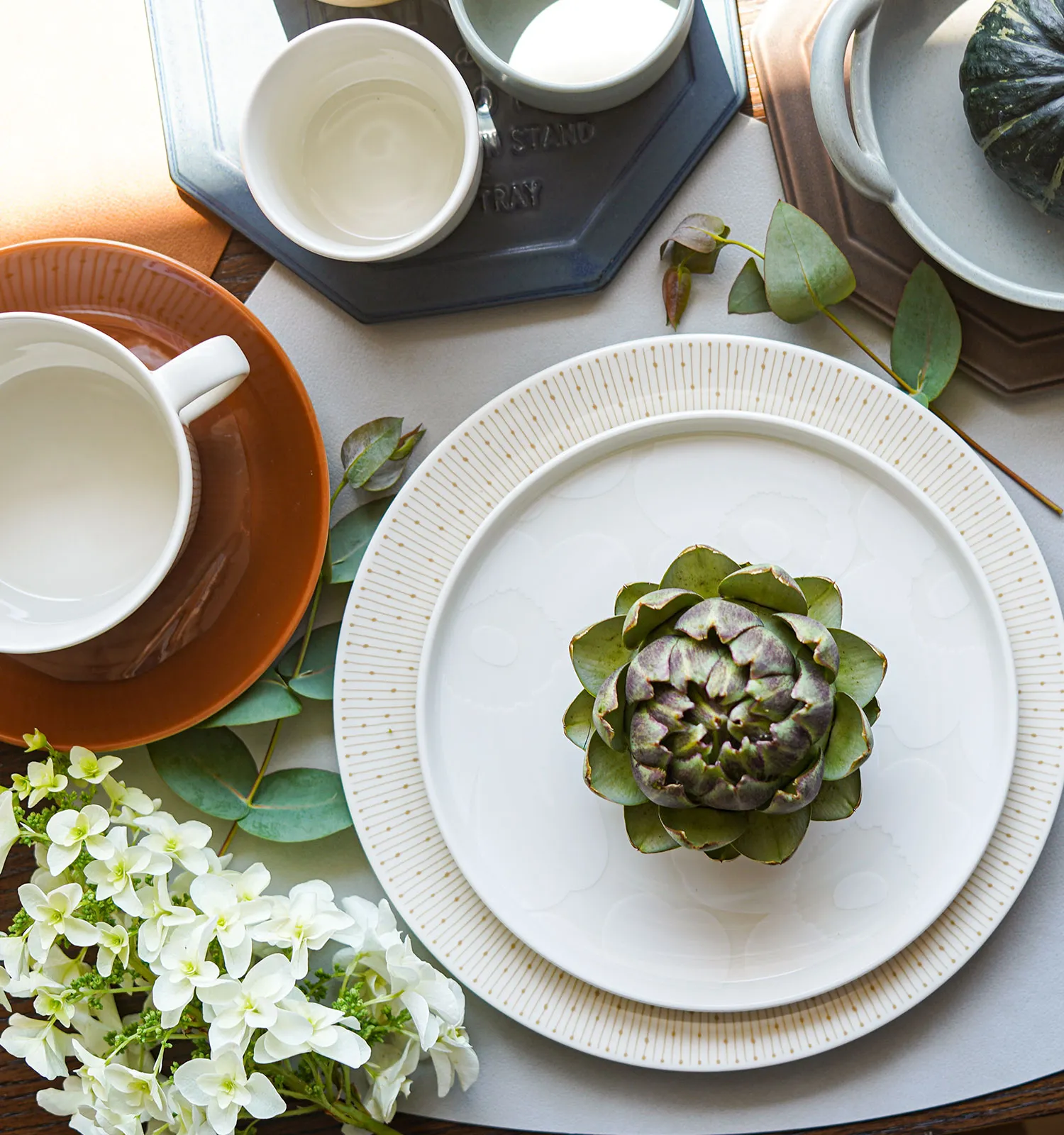 秋のテーブルコーディネート：ドットパターンの白プレートにアーティチョーク、テラコッタ色のC&S、かぼちゃを盛った器、ユーカリの葉、白いあじさい、カトラリー