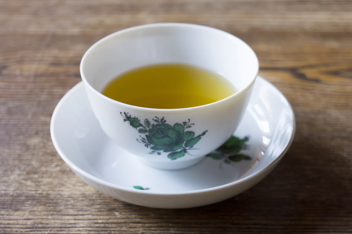 アウガルテン マリアテレジア グリーン 茶杯＆ソーサーと注がれた緑茶 ─ 木のテーブル、静かな机上