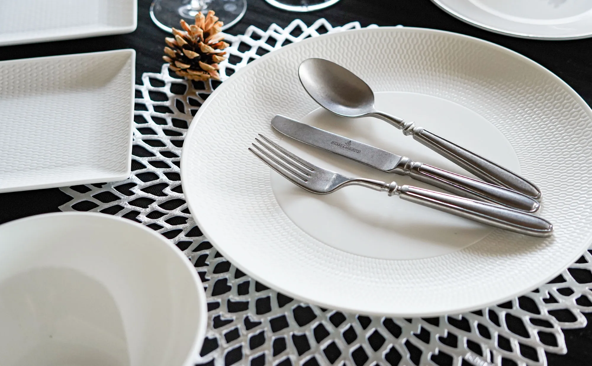 白いディナープレートの上にアンティーク調の銀のナイフ・フォーク・スプーン、白いボウルと四角皿、松ぼっくり