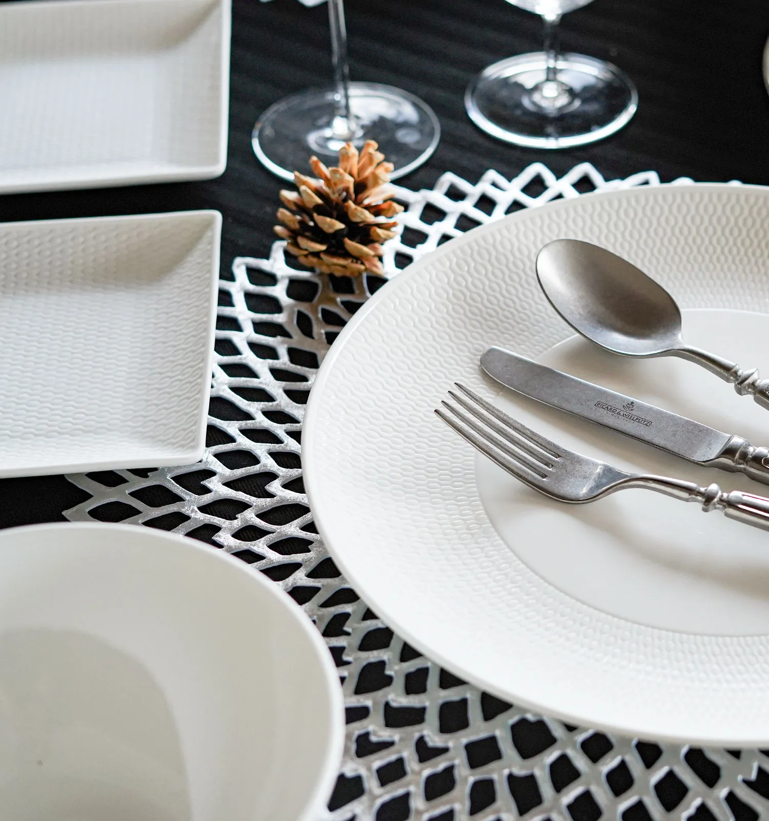 白いディナープレートの上にアンティーク調の銀のナイフ・フォーク・スプーン、白いボウルと四角皿、松ぼっくり